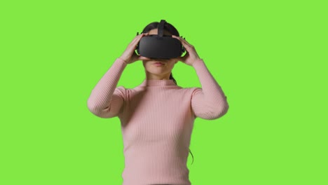 Frau-Setzt-Virtual-Reality-Headset-Auf-Und-Interagiert-Vor-Grünem-Studiohintergrund